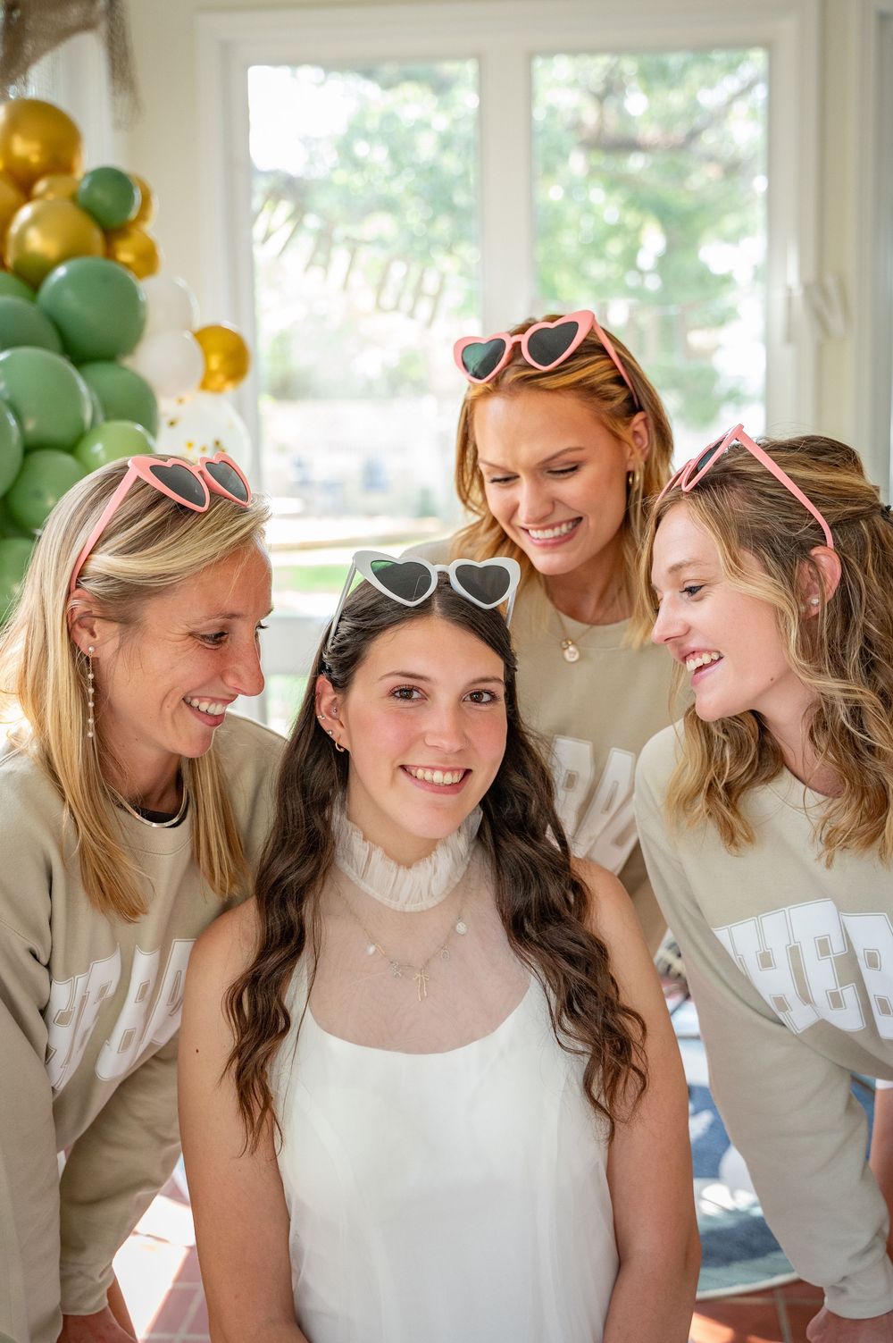 A festive gathering with green and gold balloon decorations in a sunlit room.