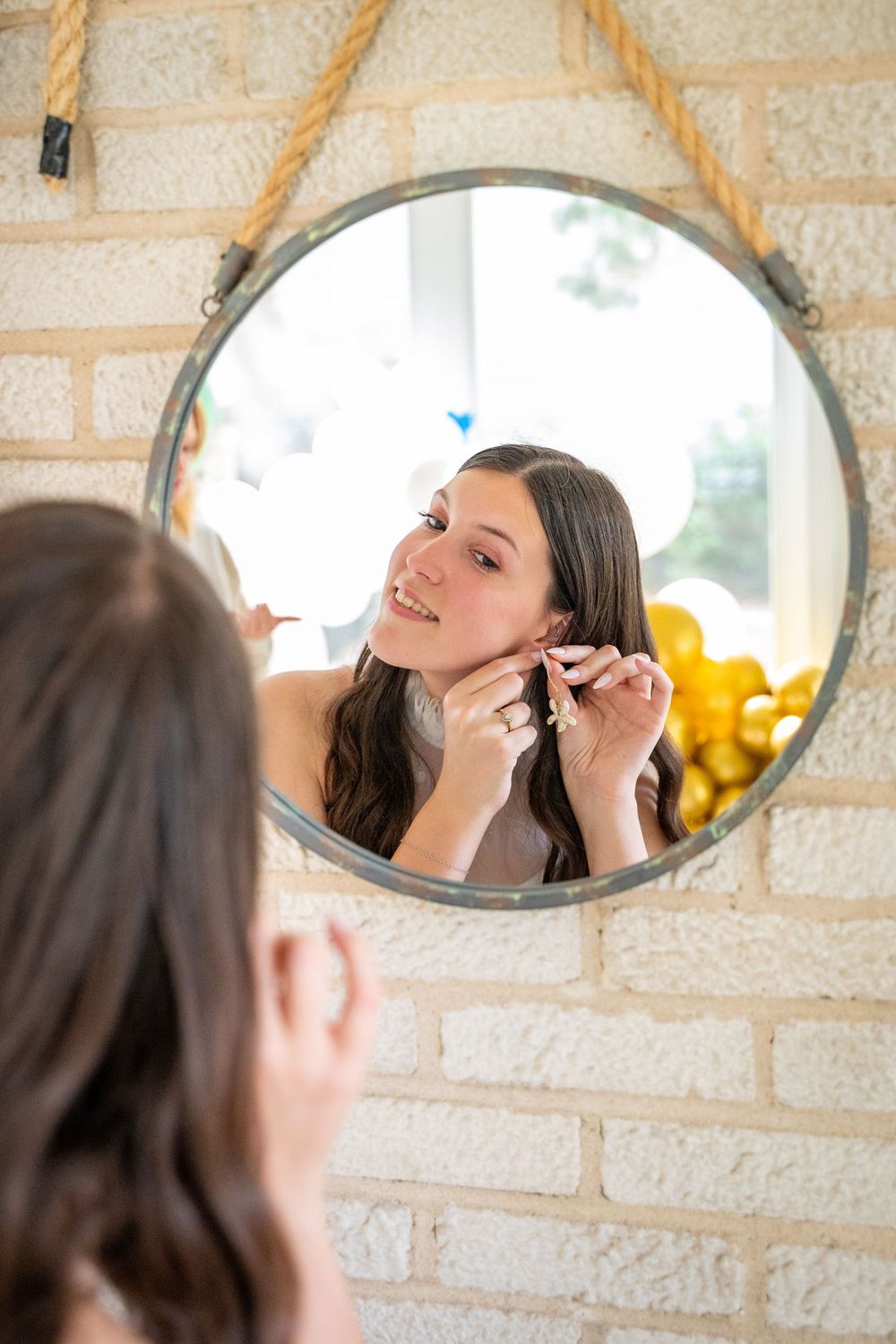 A person putting on earrings while looking in a round mirror mounted on a brick wall.