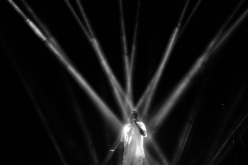 Dramatic black and white concert lighting beams shine through smoke creating striking patterns on a dark stage.