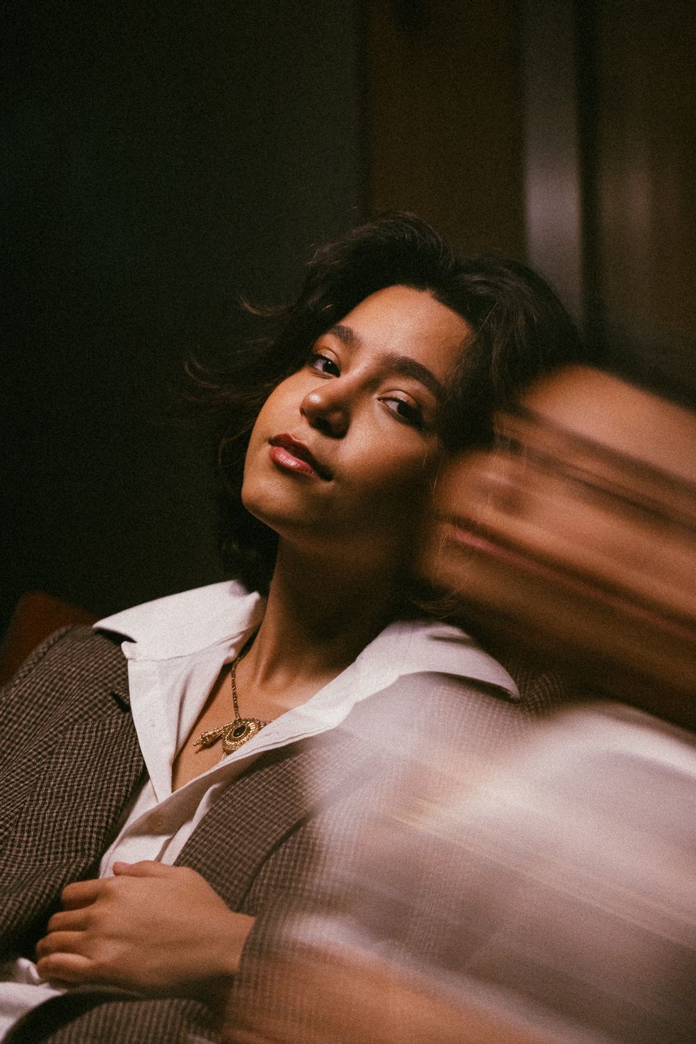 A dramatic portrait series showing someone in a white collar and brown blazer against dark shadows and warm lighting.