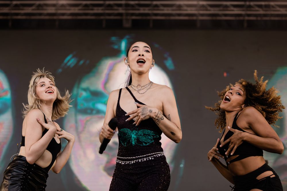 Dancers in black outfits perform energetic dance moves against a dark background with blue lighting effects.