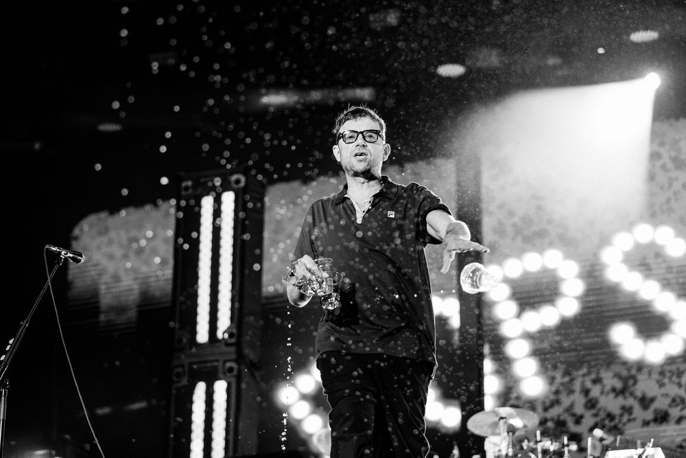 A performer in dark clothing stands on stage surrounded by glittering lights and sparkles during a concert performance.