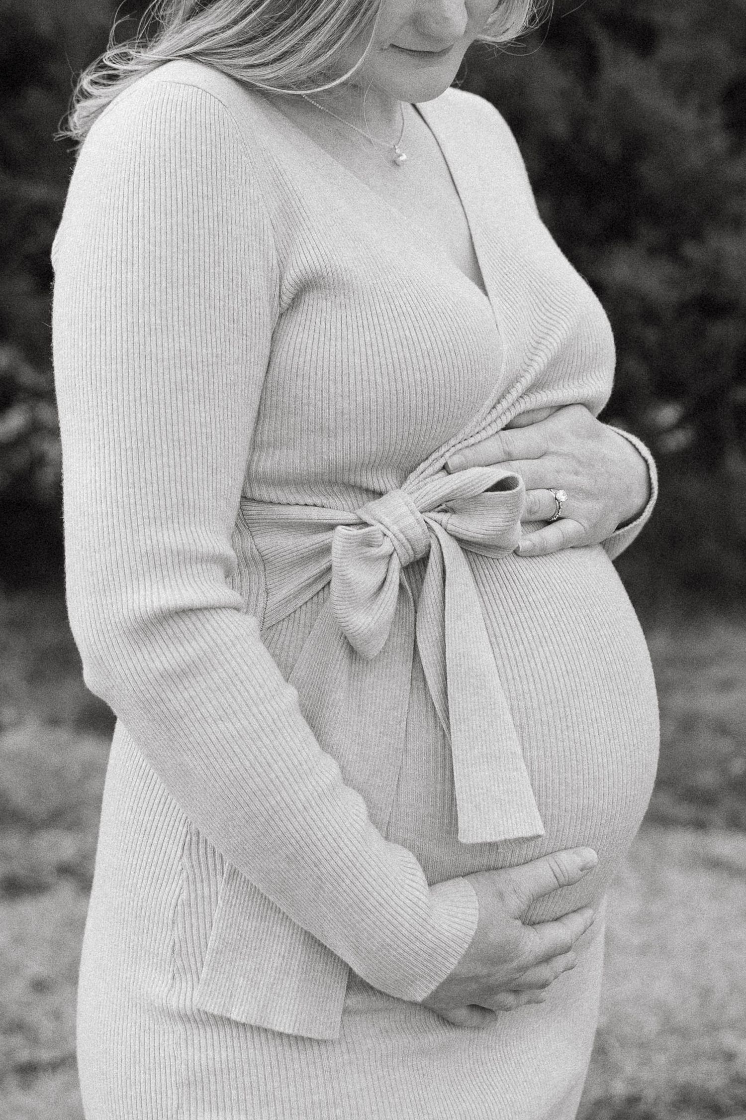 pregnant mother holds her baby bump and looks down front of lake olathe during photo session