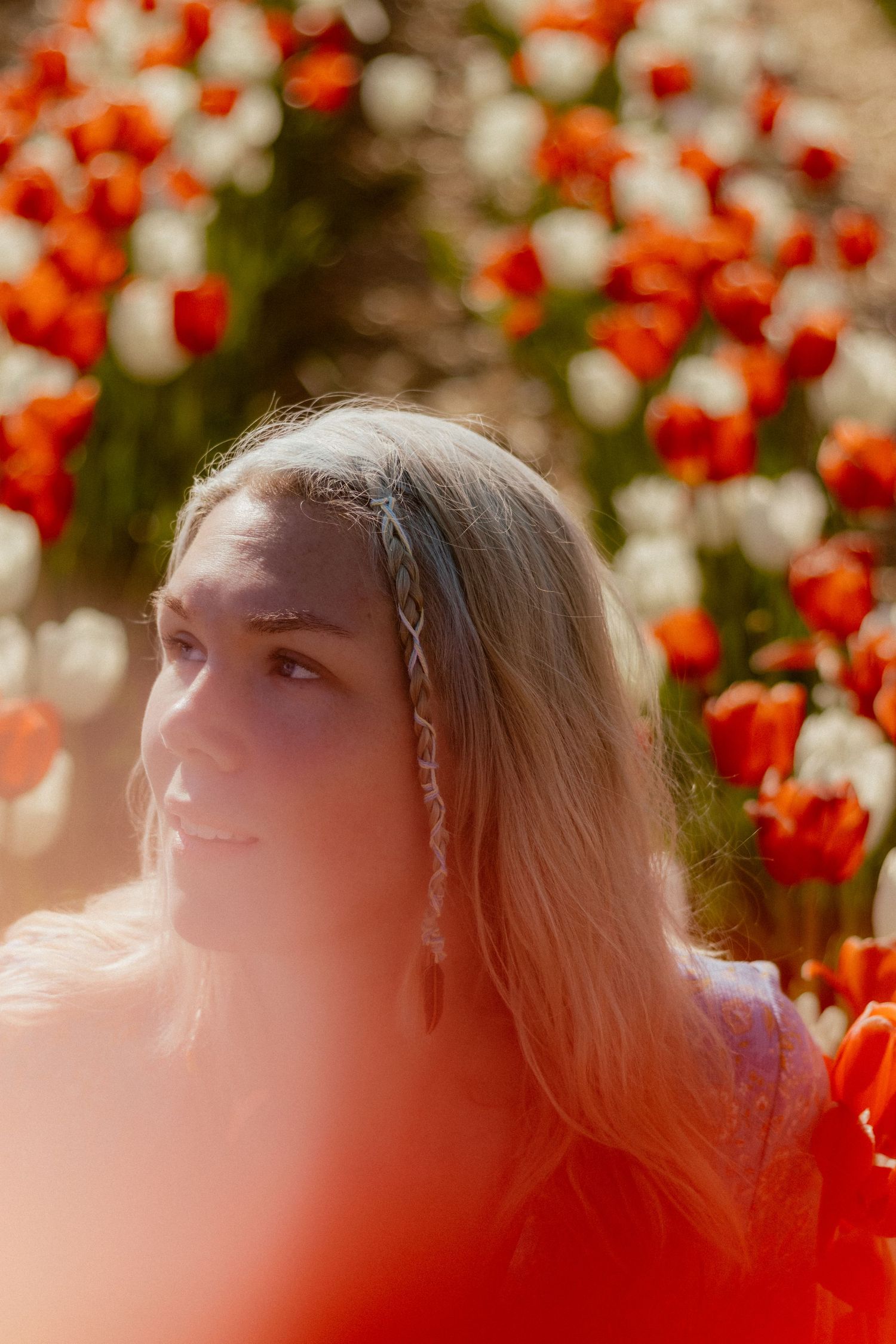 Dreamy portrait in a garden with red flowers and soft sunlit bokeh effects.