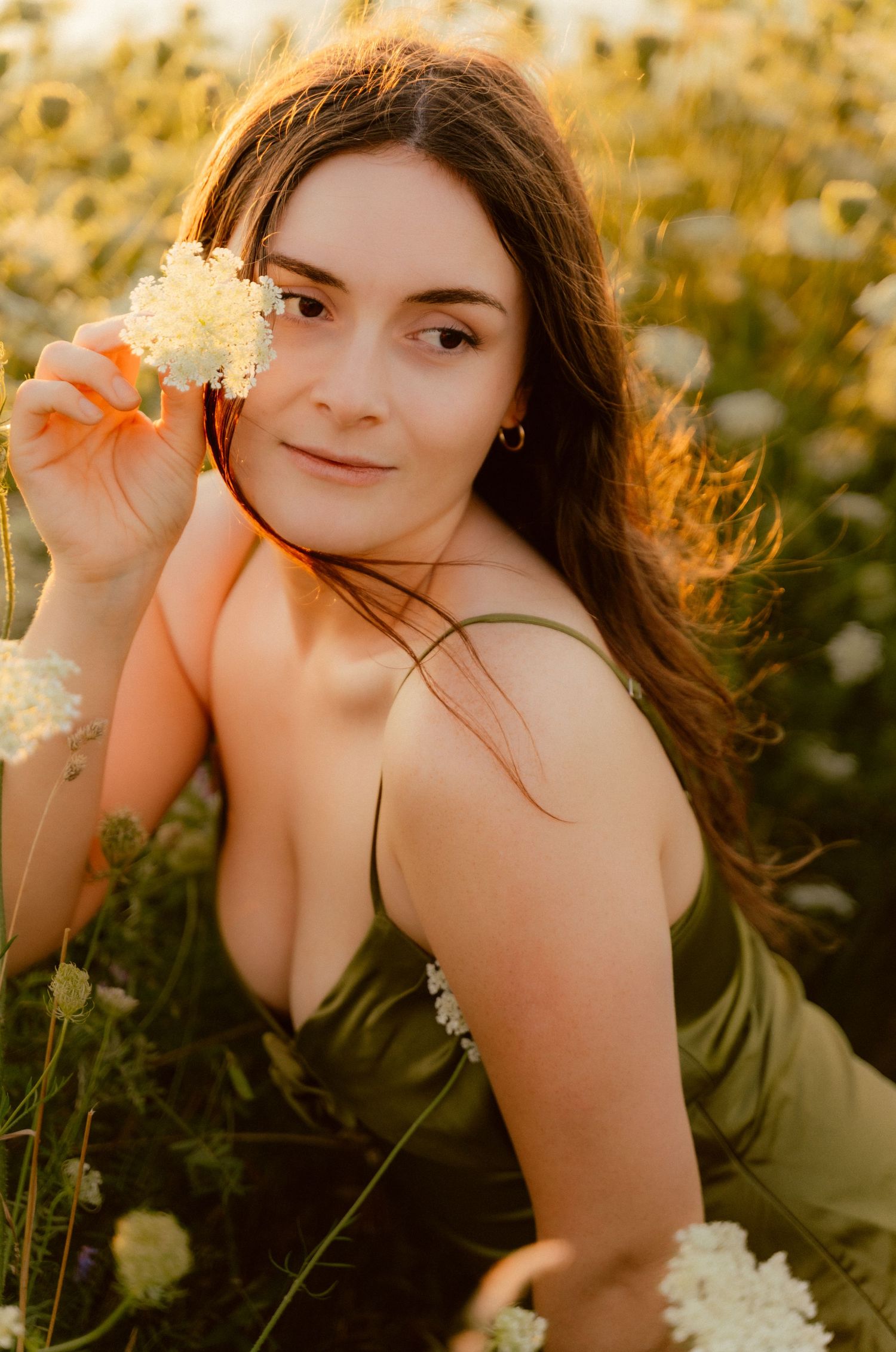 Portrait in sunflower field during golden hour holding white wildflower.