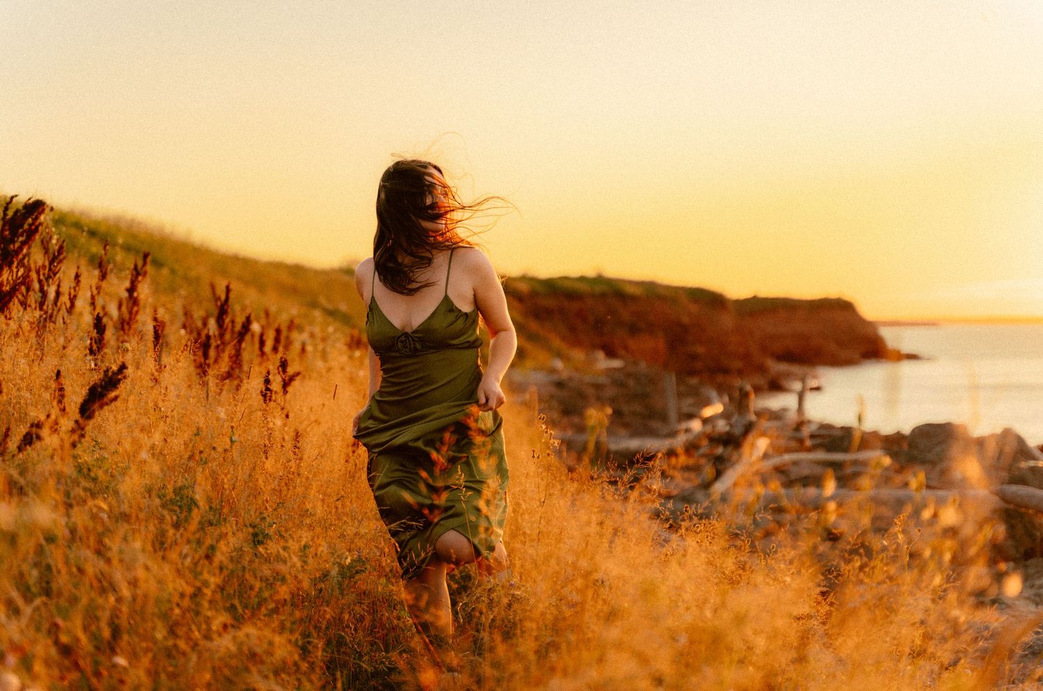 Silhouette walking through tall grass on coastal cliff during golden hour.