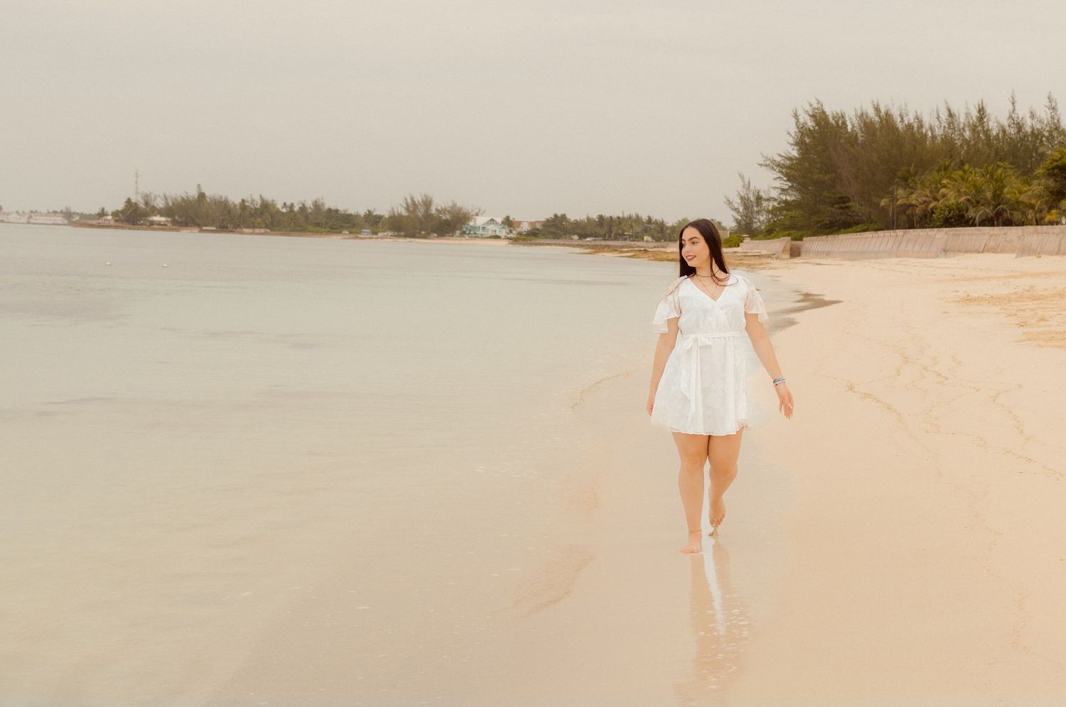 Person in white dress walking along serene beach at sunset.