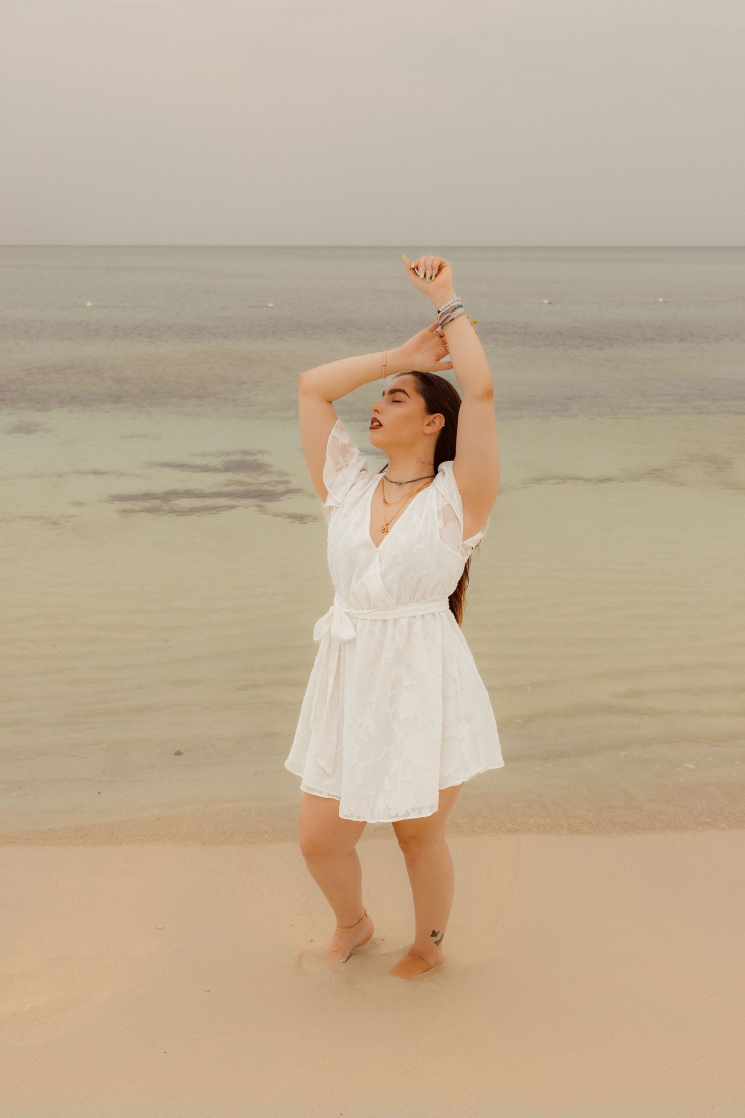 Dancing figure in white dress on peaceful beach during golden hour.