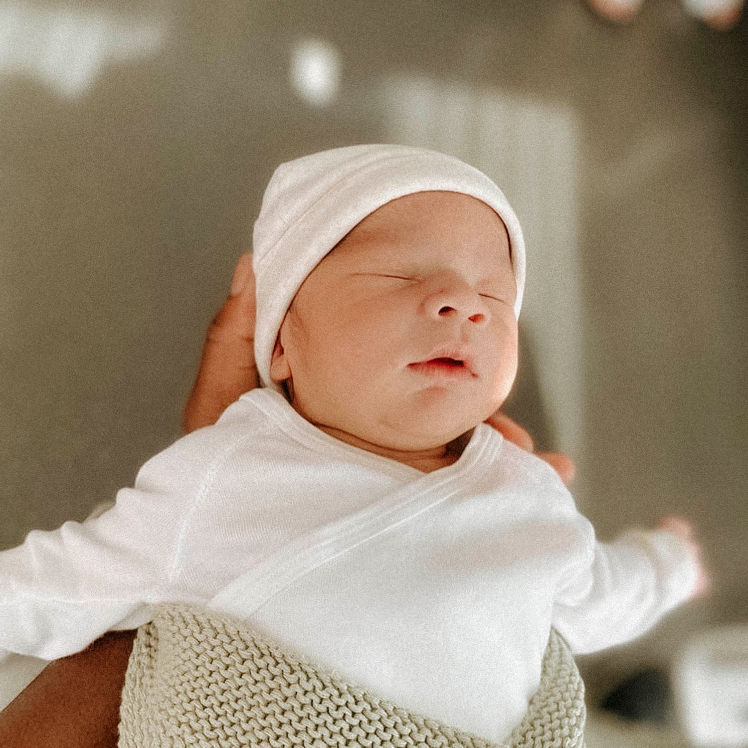 A newborn baby in white clothing and hat sleeping peacefully.