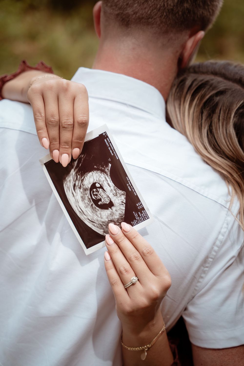 Mother holding ultrasound photo while embracing partner during maternity session.