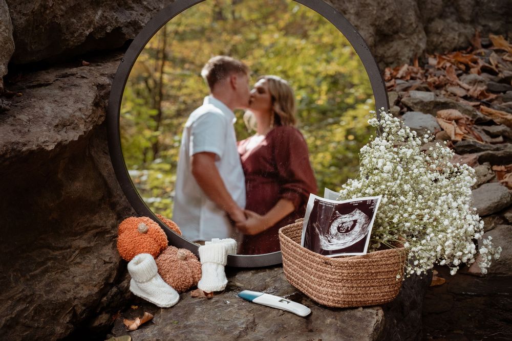Reflection of expecting couple in a mirror with baby announcement props.