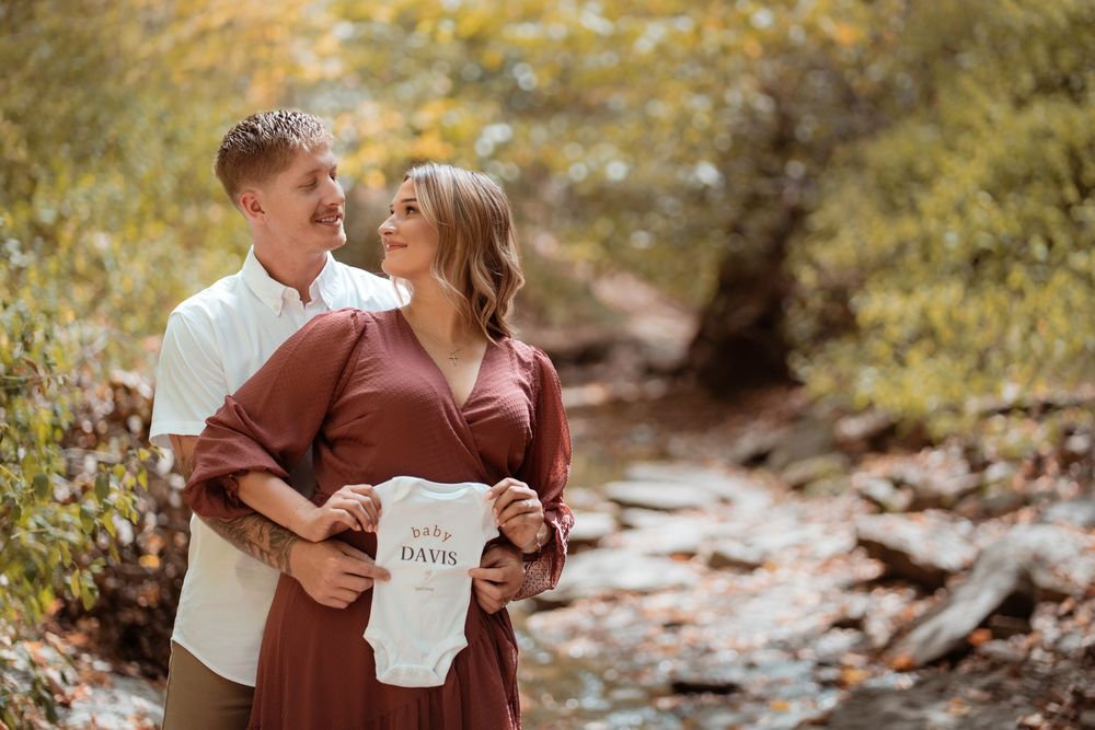 Expecting couple embracing beside a creek during a fall maternity session.