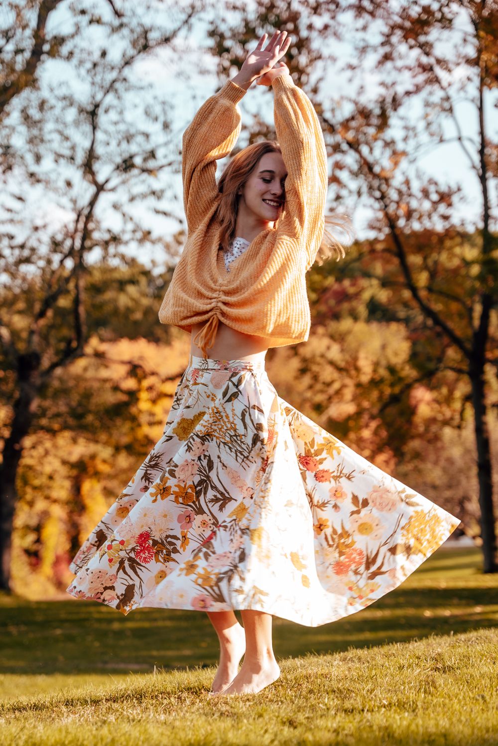 Woman twirling in a floral dress during a golden hour senior portrait session.