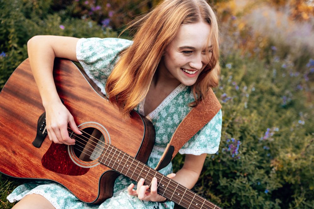 Senior portrait featuring acoustic guitar in a flower garden.