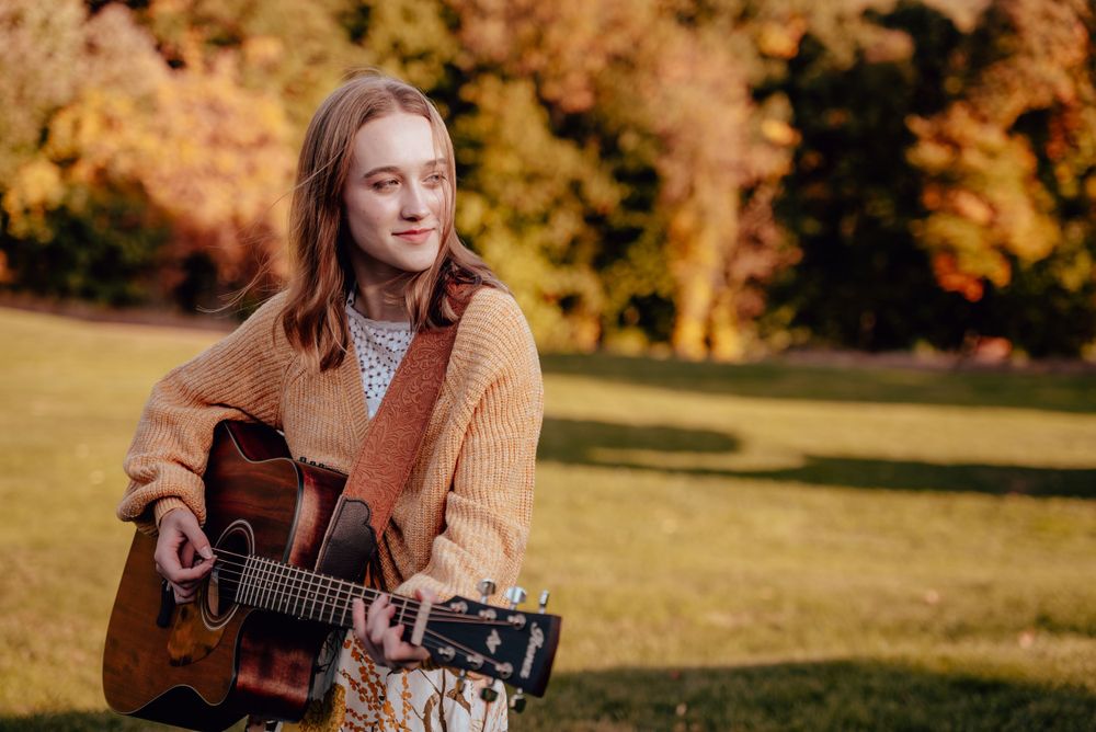 Musician playing acoustic guitar during an outdoor senior portrait session.