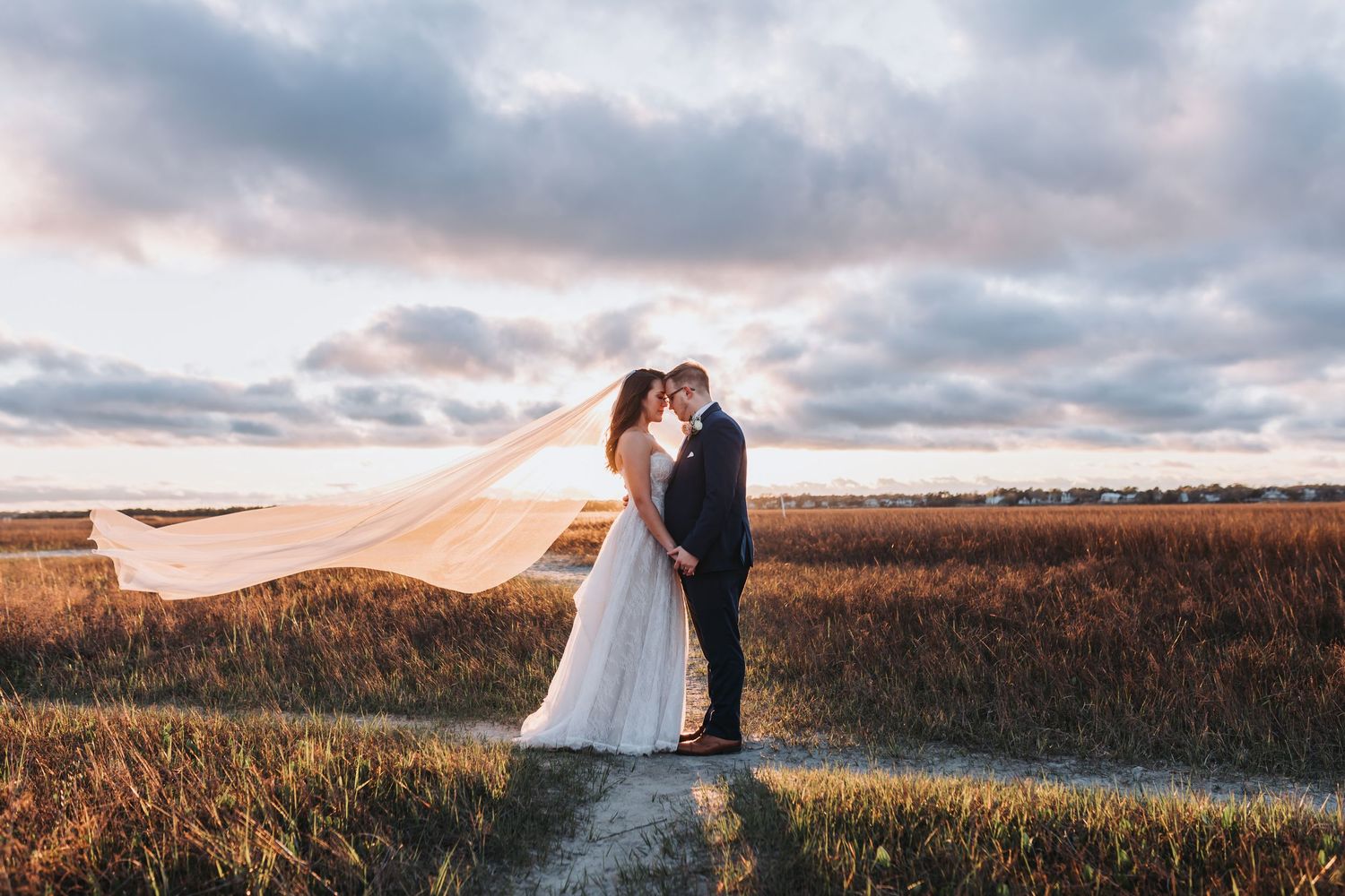 Couple stands close together on grassy shore overlooking calm water at dusk.