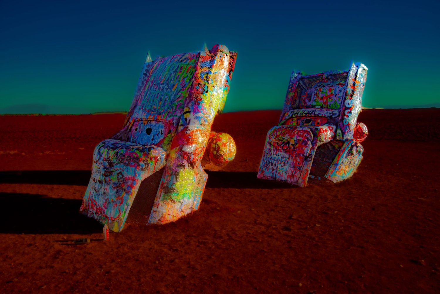 Colorful spray-painted Cadillac cars arranged in desert landscape at sunset.