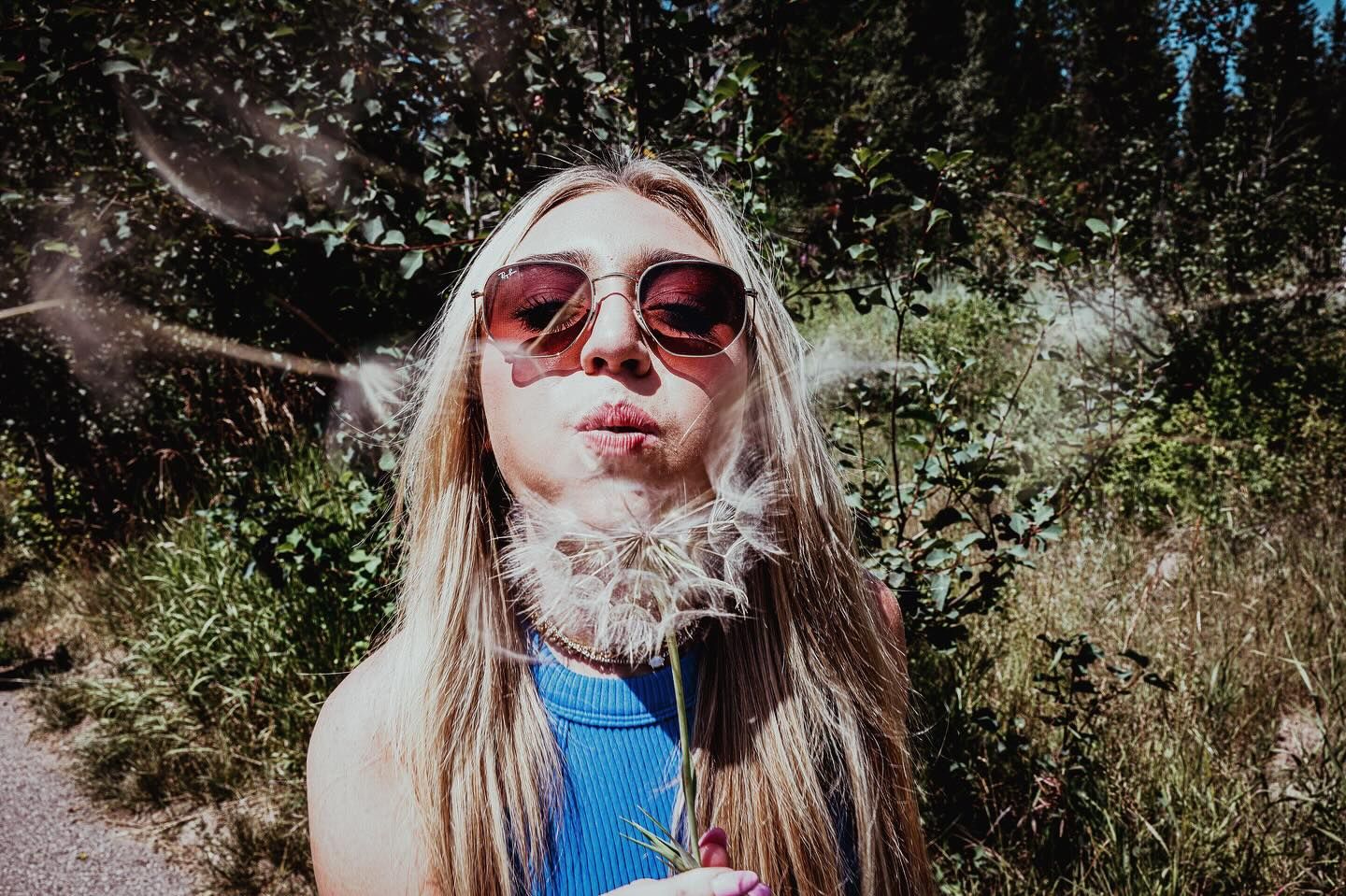 Person blowing smoke while wearing red sunglasses outdoors on a sunny day.