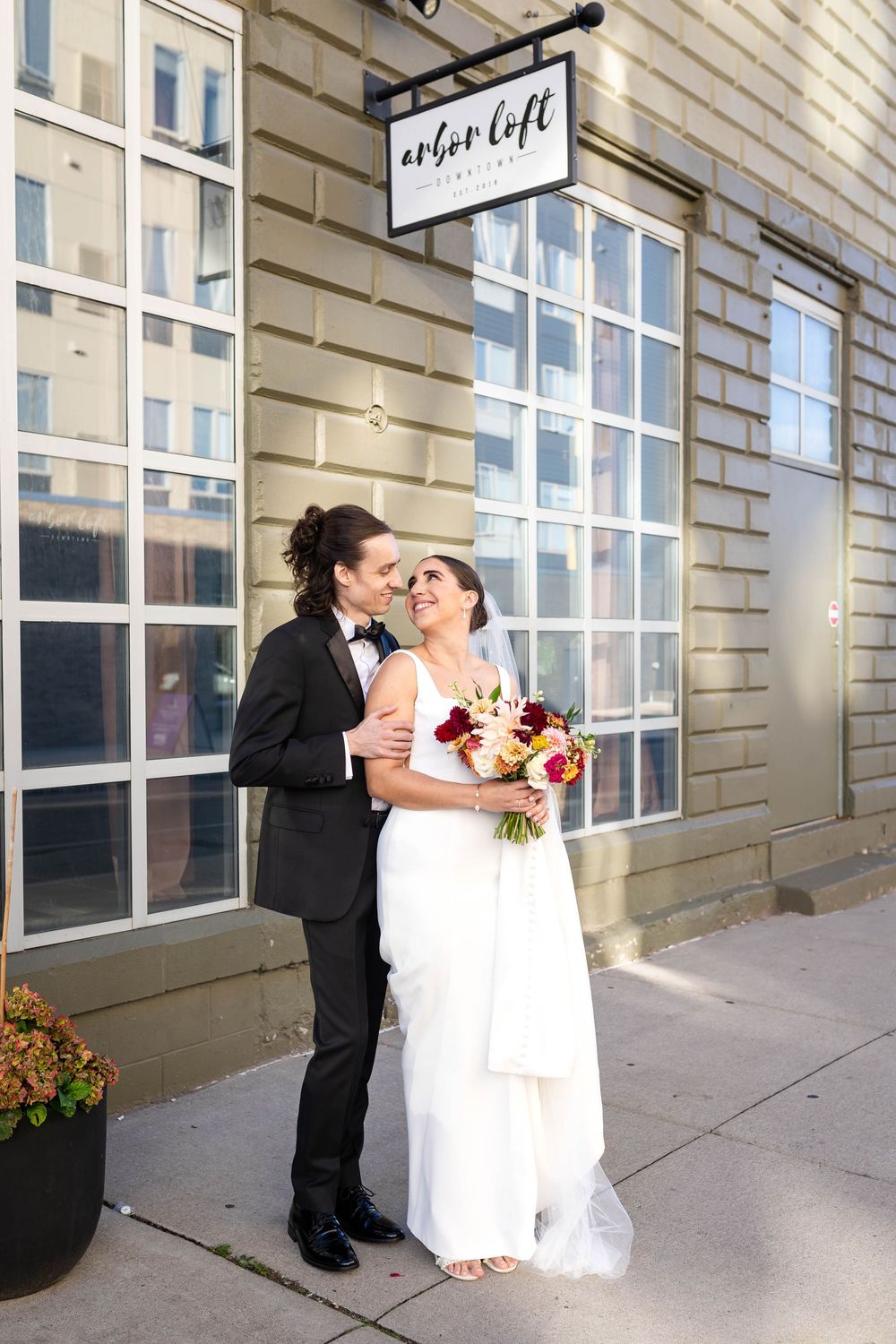 Newlywed couple shares intimate moment outside Urban Loft venue with brick walls and large windows in background.