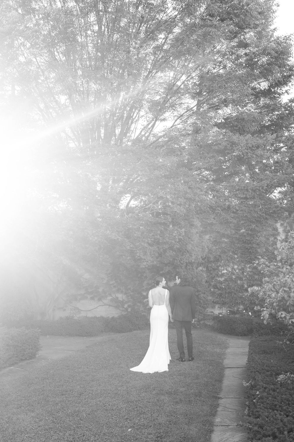 A romantic black and white photo of a couple standing on a misty garden path surrounded by trees.