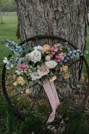Beautiful wedding bouquet with roses and blue flowers arranged on a rustic wagon wheel.