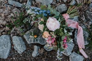Wedding bouquet with pink ribbon laying on rocky ground.