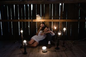 Couple embracing on wooden floor surrounded by candlelight and hanging lamps.