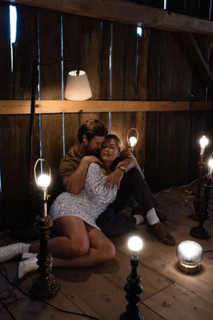 Romantic moment captured in dimly lit barn with vintage lighting fixtures.