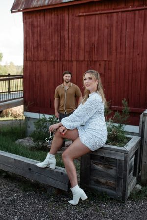 A rustic barn photoshoot featuring two people in casual attire posing against red wooden siding.