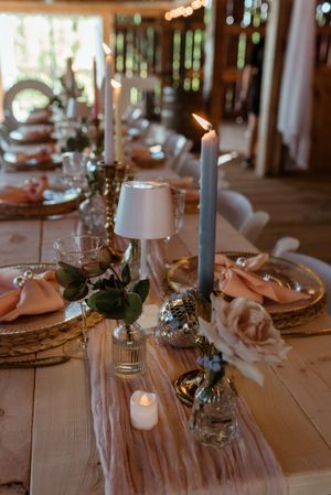 Elegant table setting with candles, small lamps, and floral arrangements on a wooden farmhouse table.
