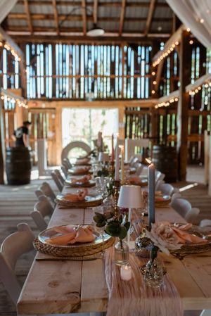 Wedding reception table setup in a rustic barn venue with string lights and natural lighting.