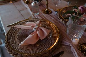 Close-up of a place setting with a peach napkin bow on a gold charger plate.