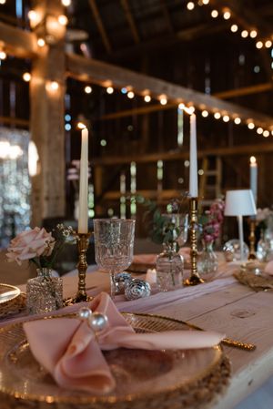 Romantic barn wedding table with string lights, tapered candles, and peach-colored napkins.