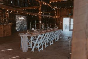 Reception venue interior showing a long table setup with white chairs and ambient string lighting.