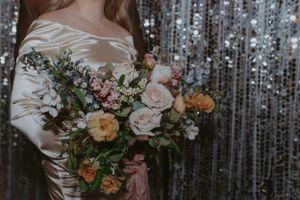 A detailed shot of a romantic bouquet with pink and peach roses against a silver sequin backdrop.