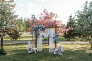 A wooden wedding arch adorned with blue flowers and white draping creates a romantic ceremony backdrop.