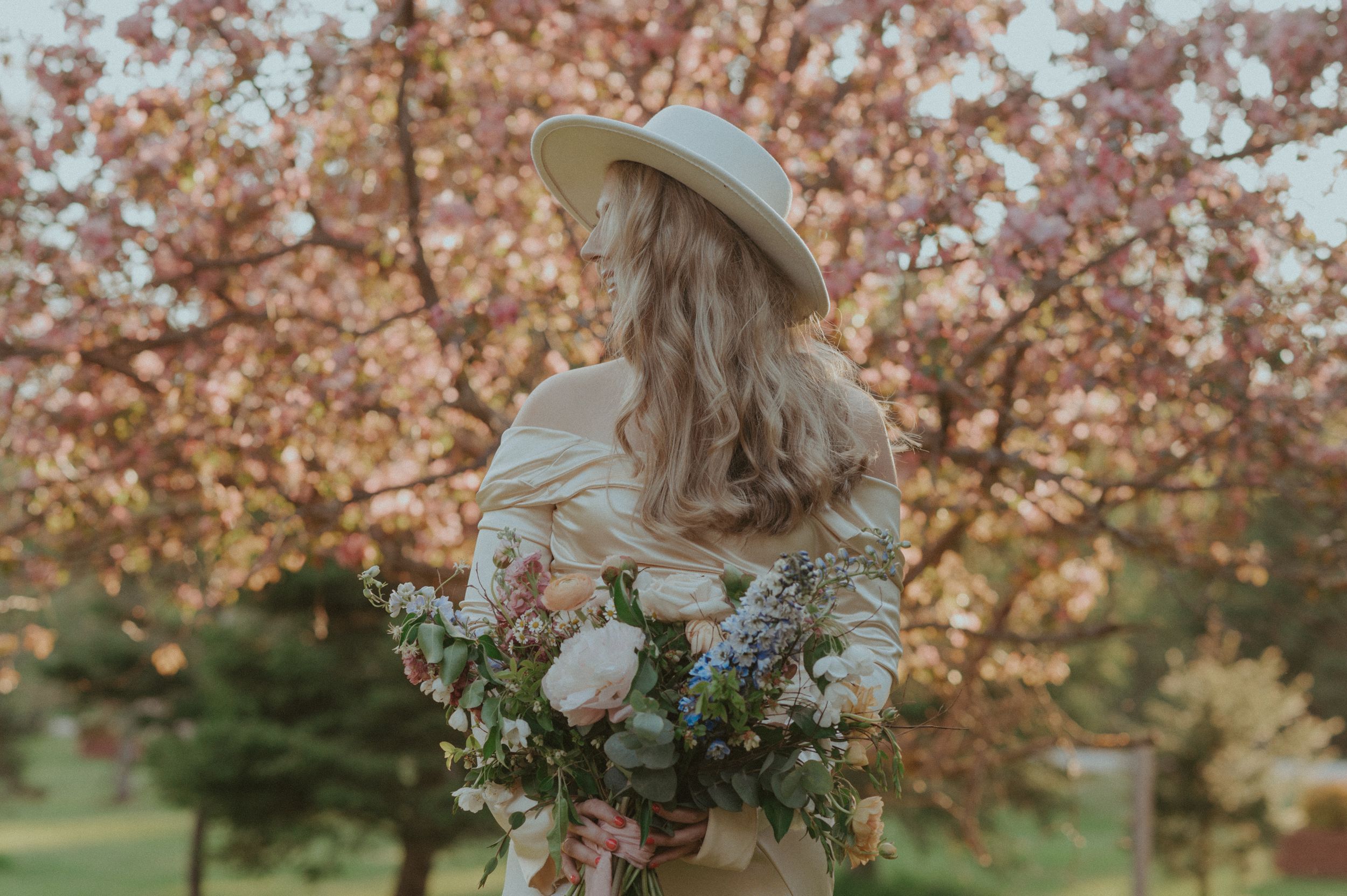 Soft feminine portrait with pink cherry blossoms and an elegant off-shoulder cream dress.