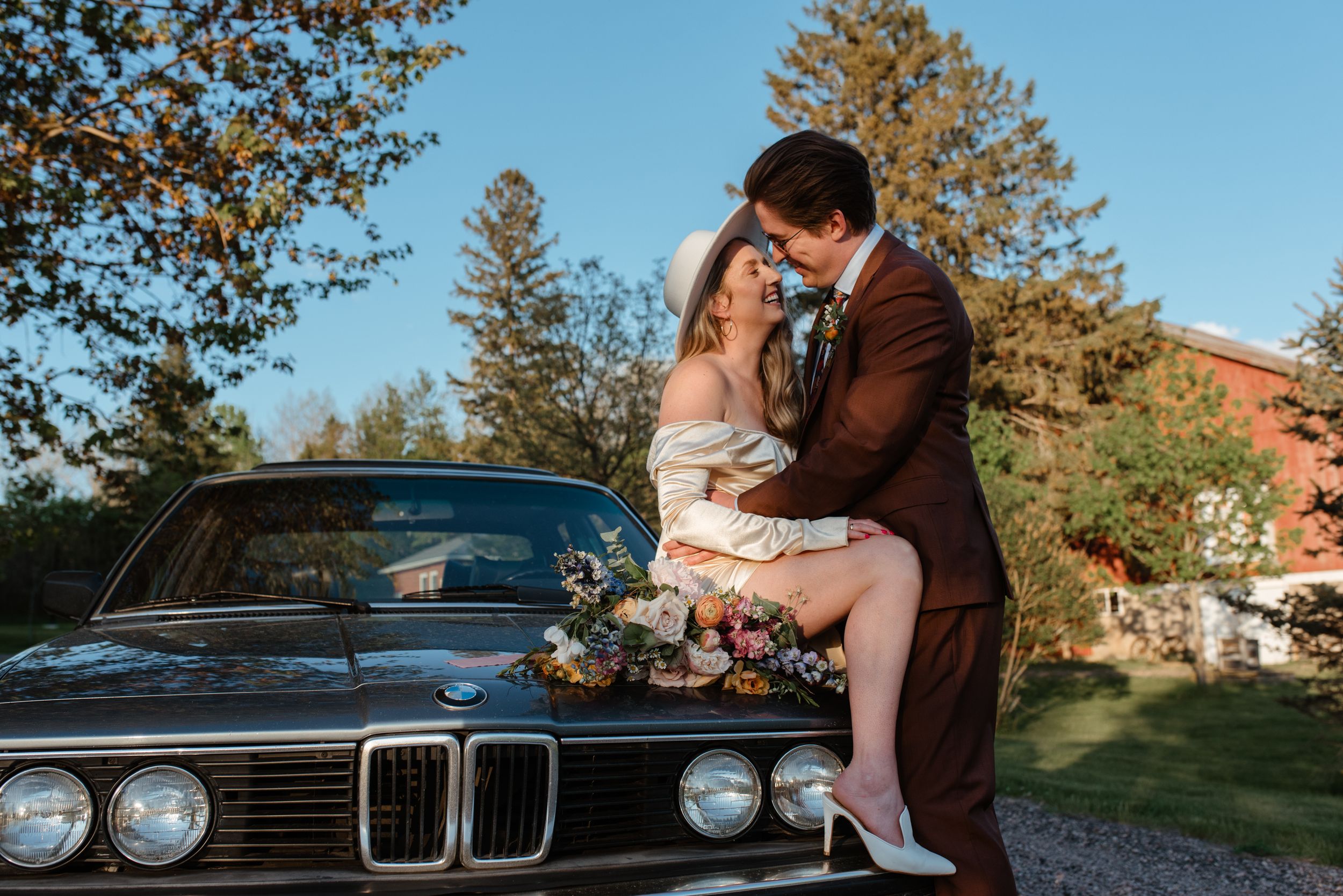 Romantic vintage-inspired wedding photo with classic BMW car backdrop.