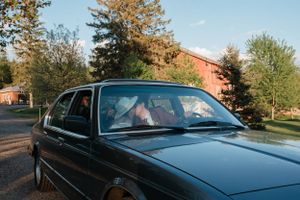 A vintage BMW sedan photographed during golden hour with a red barn visible in the background.
