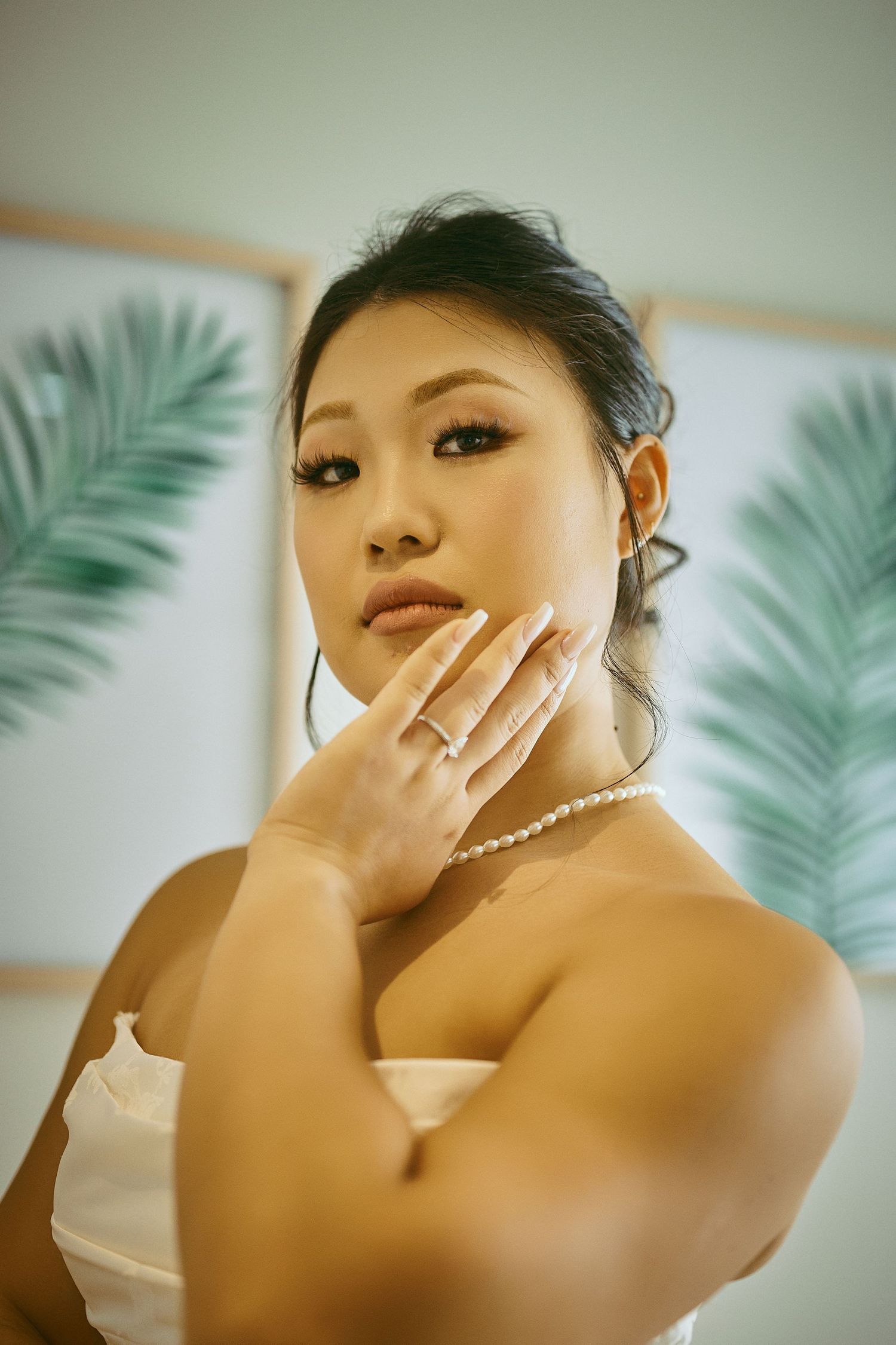 Elegant bride in strapless white gown wearing pearl necklace and ring, posing gracefully with hand on face. Jamaican Wedding Photographer