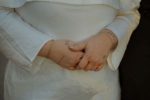 Hands clasped together against a white dress fabric, showing delicate sleeve details and bracelet.