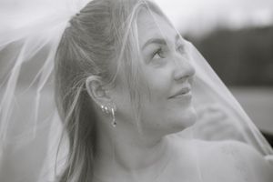 Black and white photograph of a bride wearing a veil and earrings as she looks up with a joyful expression.