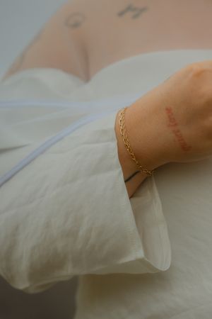 A close-up shot of a delicate gold chain bracelet against white fabric.