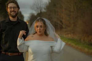 A couple poses on a country road during a fall wedding photoshoot, bride wearing an elegant off-shoulder white gown.