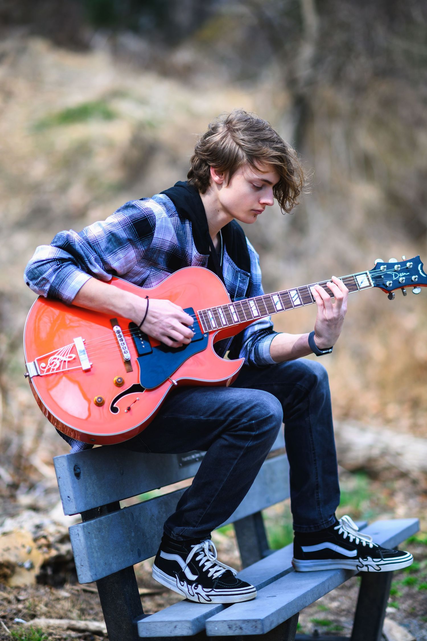 Young musician in plaid shirt playing orange electric guitar while sitting outdoors on wooden steps.