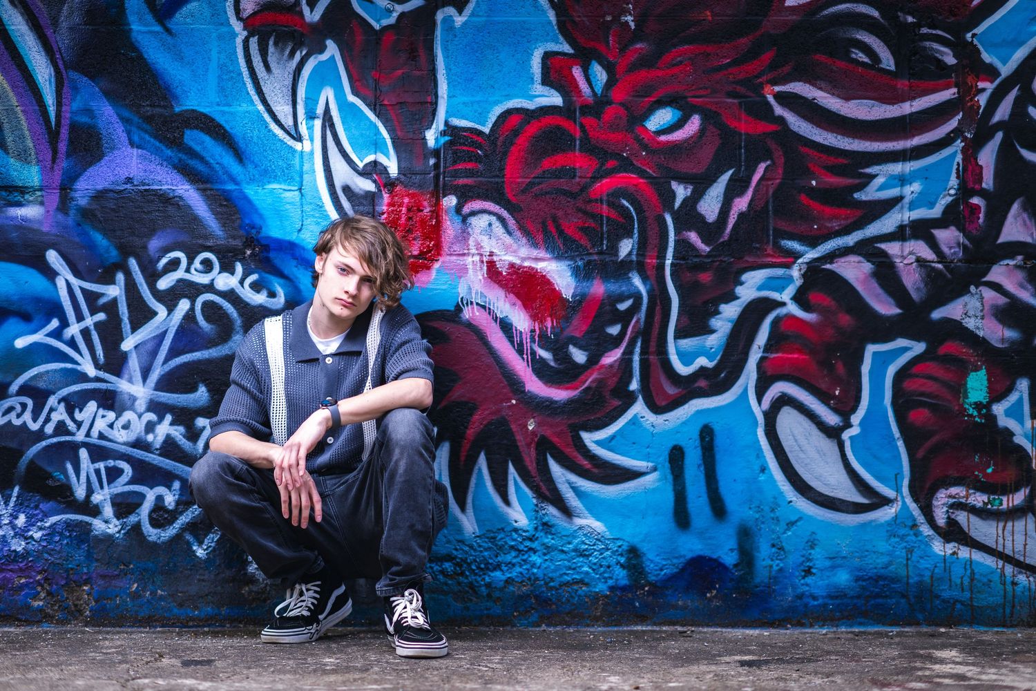 An edgy photoshoot against a vibrant graffiti wall featuring red and blue monster artwork.