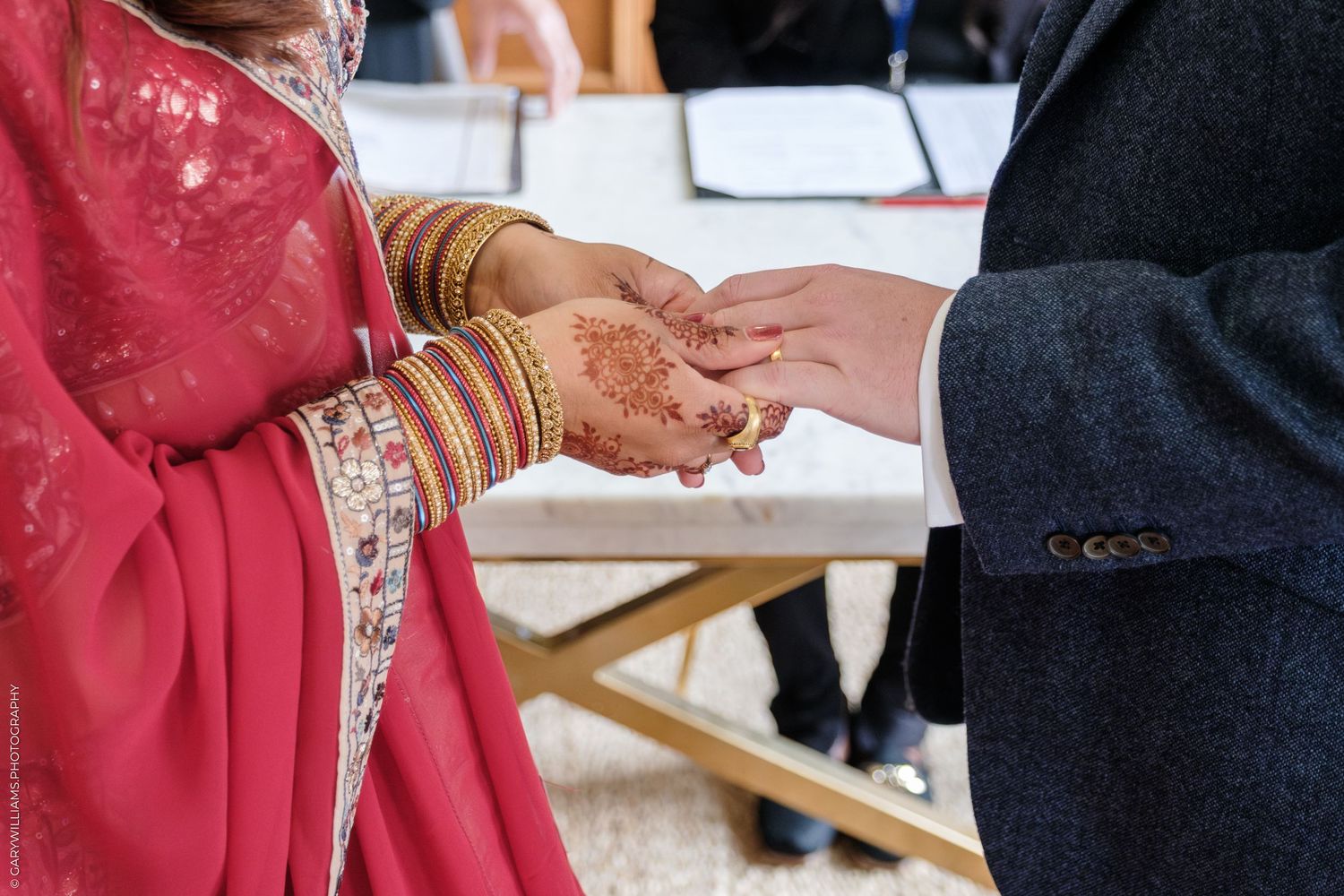 Close up of hands exchanging rings during traditional Indian wedding ceremony with red and gold details.