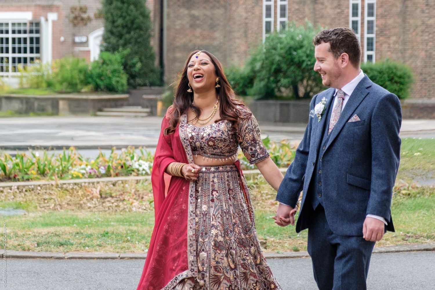 A couple shares a joyful moment outdoors, with one wearing a brown sequined dress and red shawl.