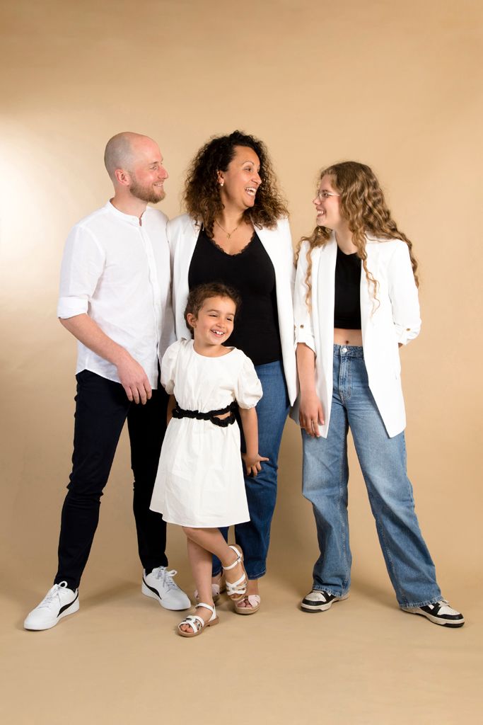 A family of four poses together in casual attire against a beige studio background.