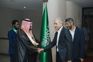 A diplomatic handshake between Saudi and Western officials with the Saudi Arabian flag visible in the background.